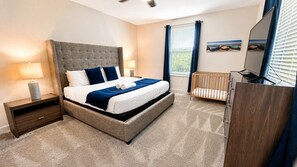 A bedroom with a bed, nightstands, a crib, a television, and a window with curtains.