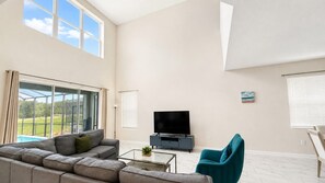 A modern living room with a large window, a flat-screen TV, a sofa, a coffee table, and a teal armchair.