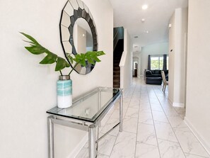 A hallway with a glass console table, a decorative mirror, and a potted plant.