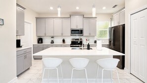 A modern kitchen with white cabinetry, a central island with bar stools, a refrigerator, and a microwave.