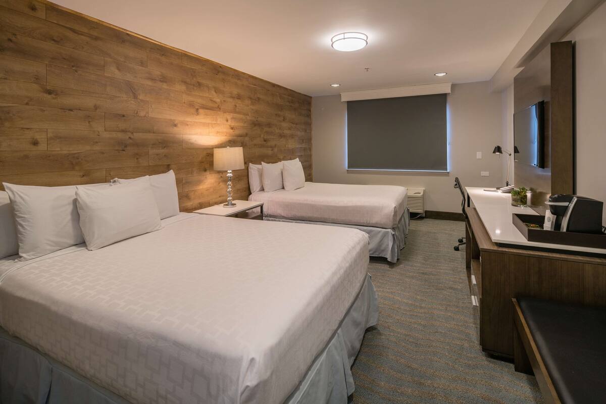 A hotel room with two beds, a desk, a chair, a TV, and a window.
