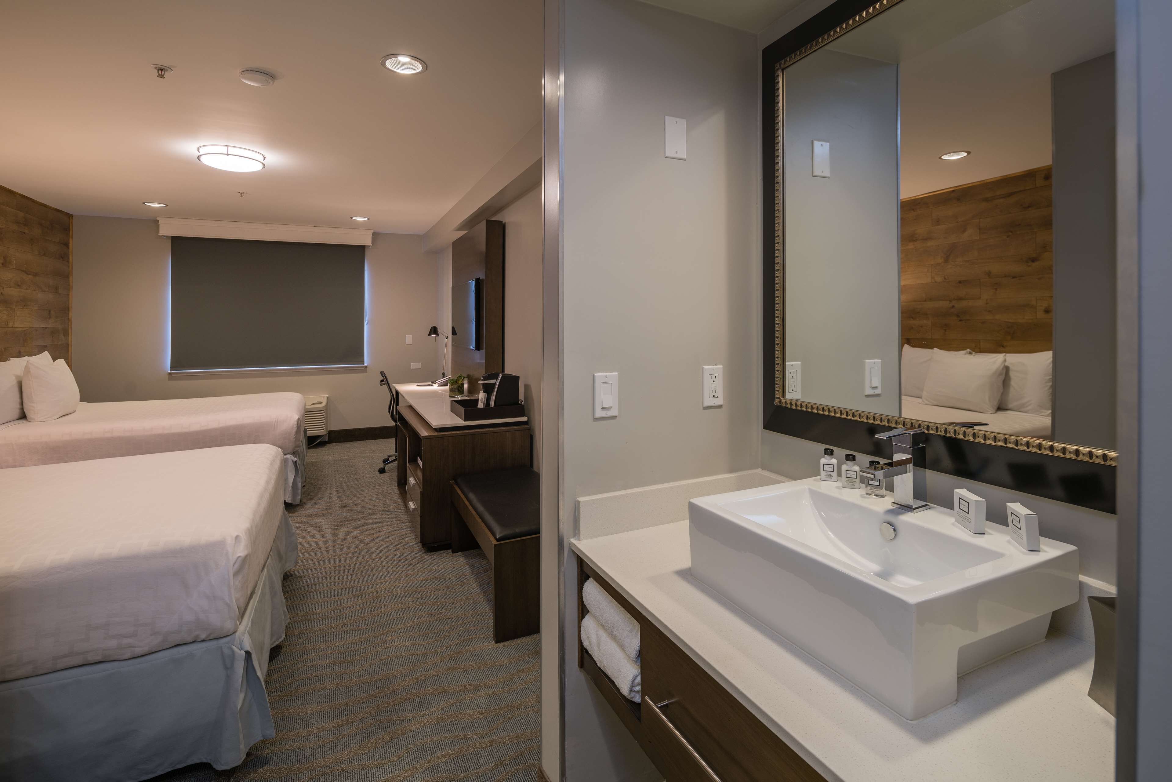 Habitación de hotel con dos camas, un espejo grande, un lavamanos y una ventana.