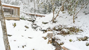 Un banco de madera en un espacio exterior nevado con un arroyo y árboles.