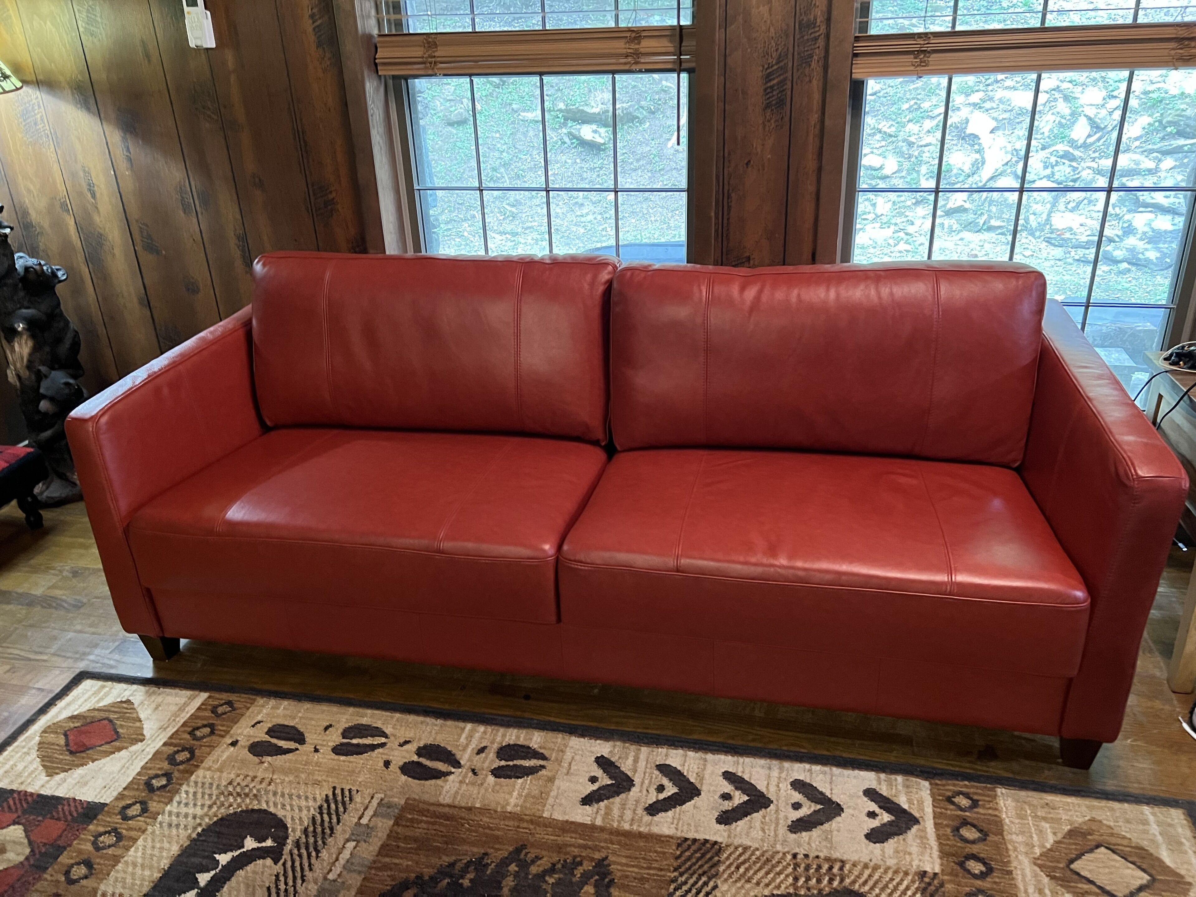 Un sofá de cuero rojo en una habitación con paredes de madera y ventanas amplias.