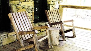 Dos mecedoras de madera en una terraza de madera con un muro de piedra al fondo.