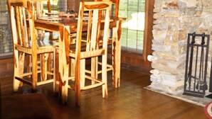 Un comedor con mesa y sillas de madera, pared de piedra y vista a través de amplios ventanales.