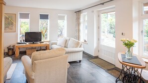 A living room with a television, sofa, and a dining area with a table and vase. - 3 bedroom accommodation in Forden (Forden)