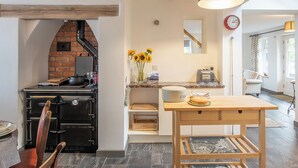 A kitchen with a brick oven, wooden beams, a wooden table, and a vase of sunflowers. - 3 bedroom accommodation in Forden (Forden)