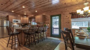A wooden cabin interior with a kitchen, dining area, and a large window.