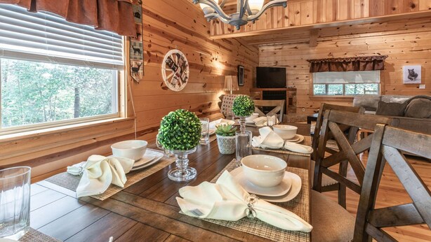 A wooden cabin interior with a dining table set for four, a television, and a cozy seating area.