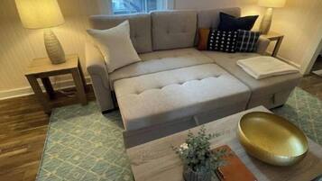 A living room with a beige sectional sofa, two side tables with lamps, a coffee table with a plant and a notebook, and a patterned rug.