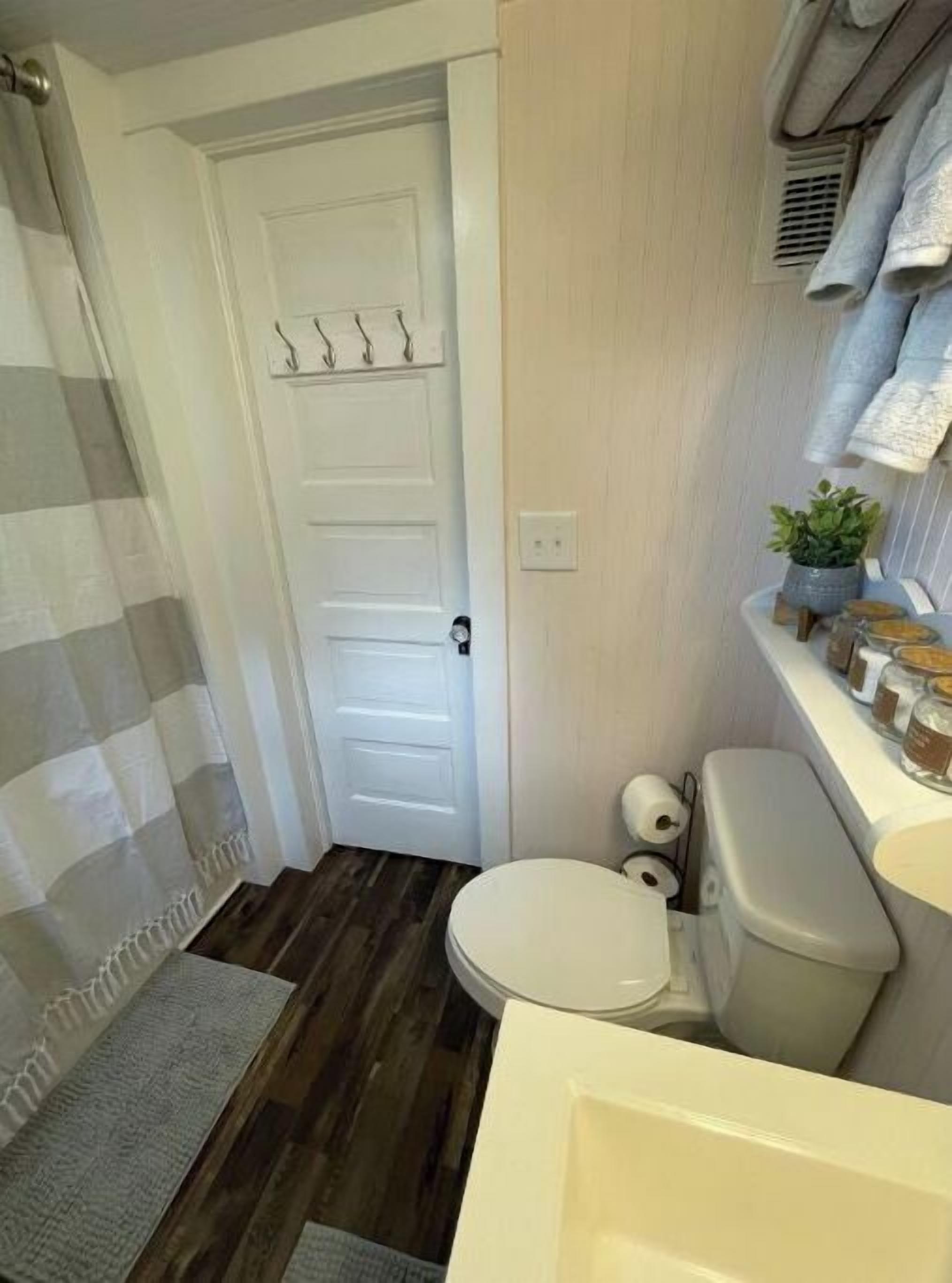 Ein kleines Badezimmer mit Toilette, Duschvorhang, Holzboden und Ablage für Pflegeprodukte.