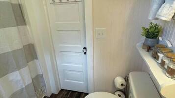 Ein kleines Badezimmer mit Toilette, Duschvorhang, Holzboden und Ablage für Pflegeprodukte.