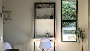 Une pièce comprenant un bureau, un lampadaire, une plante en pot et une fenêtre donnant sur des arbres.