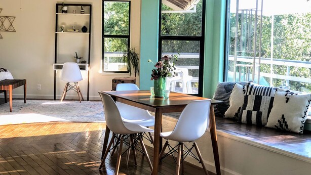 Un coin repas avec une table en bois et des chaises blanches, une bibliothèque et une fenêtre donnant sur un paysage verdoyant.