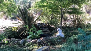 Un jardin agrémenté d’une sculpture en pierre, de différentes plantes et d’un petit étang.