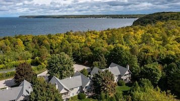 A residential area with houses surrounded by dense forest and a body of water in the background.