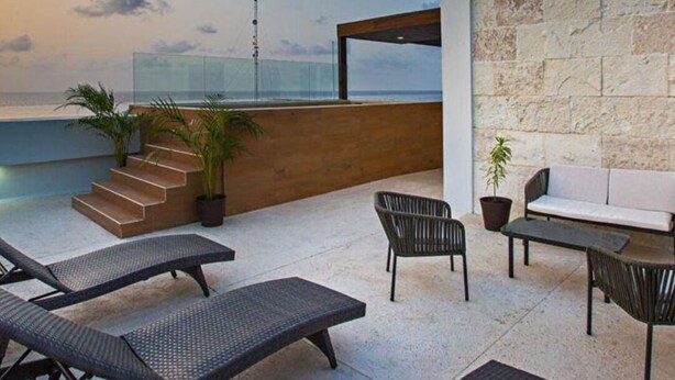 Un espace extérieur moderne aménagé avec des fauteuils et un canapé, offrant une vue sur une étendue d’eau.