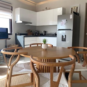 Une cuisine moderne avec des meubles blancs, un réfrigérateur en acier inoxydable et une table à manger avec des chaises en bois.