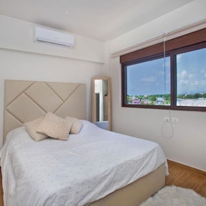 Une chambre à coucher avec un lit, une fenêtre donnant sur un beau paysage, un miroir et un appareil de climatisation.