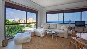 Un salon moderne avec de grandes fenêtres, un canapé, une table basse et un téléviseur.