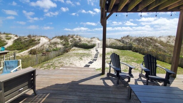 Une terrasse en bois avec des fauteuils Adirondack, une piscine et une vue sur les dunes.