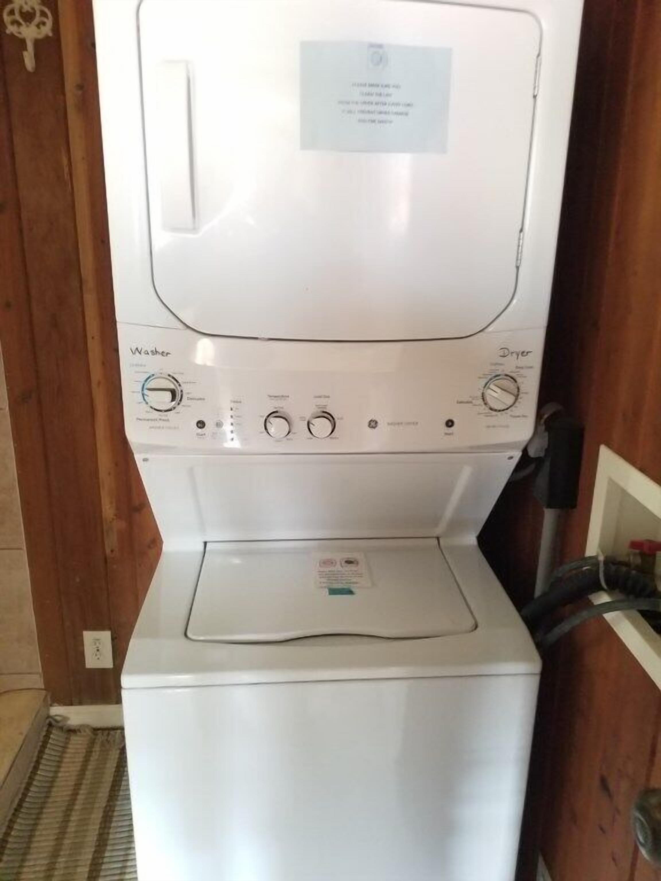 A white washer and dryer unit with a control panel, located in a room with wooden walls.