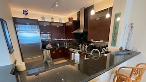 A modern kitchen with dark cabinetry, stainless steel appliances, and a central island with bar seating. - FULL TIME MGR - LUXURY PENTHOUSE - OFFERS KEY LARGO'S BEST PANORAMIC OCEAN VIEWS (Key Largo)