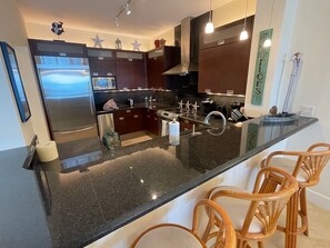 A modern kitchen with dark cabinetry, stainless steel appliances, and a central island with bar seating.