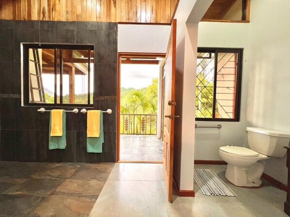 A bathroom with a toilet, a sink, and a window. There is a towel rack with towels hanging on it.