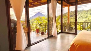 A room with a balcony overlooking a lush landscape and a mountain.