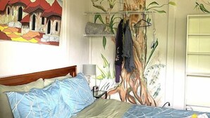 Une chambre à coucher avec un lit, une fresque murale représentant un arbre et un tableau représentant un village.