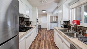 A modern kitchen with stainless steel appliances, white cabinetry, and a wooden floor.