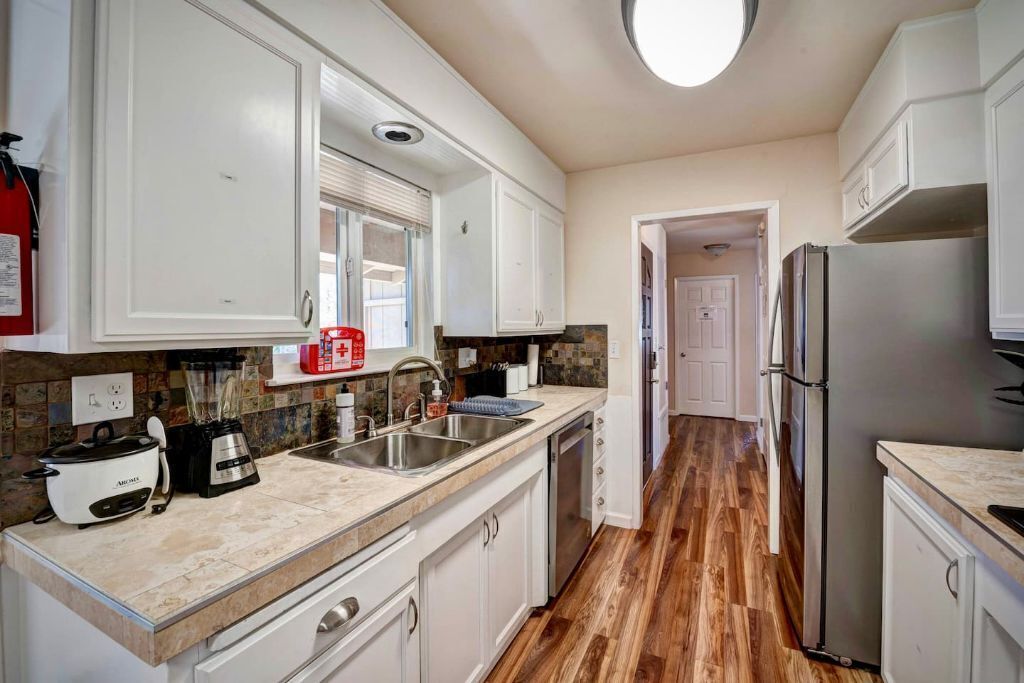 A modern kitchen with white cabinets, a granite countertop, a stainless steel refrigerator, and a built-in oven.