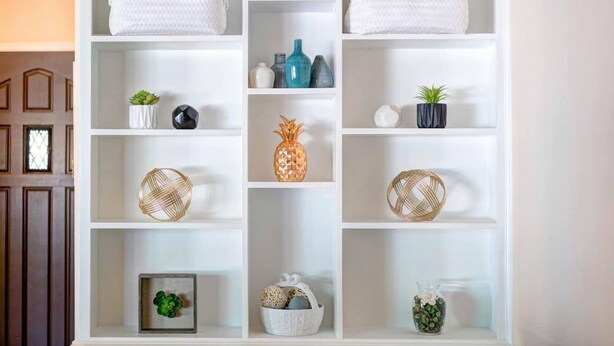 A white shelving unit with various decorative items, including woven baskets, vases, and small potted plants.
