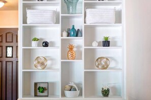 A white shelving unit with various decorative items, including woven baskets, vases, and small potted plants.