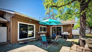 A backyard with a patio table and chairs, a grill, and a tree.