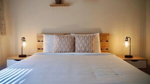 A neatly made bed with a wooden headboard, two bedside lamps, and three small wooden shelves above the bed.