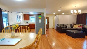 A modern living room with a dining area, wooden flooring, a sofa, and a kitchen in the background.