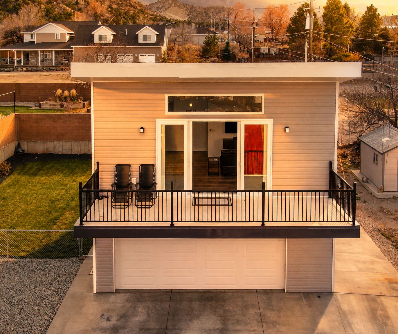 A single-story house with a garage, a balcony with chairs, and a small attached shed.