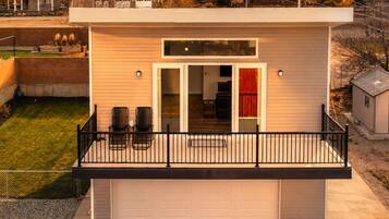 A single-story house with a garage, a balcony with chairs, and a small attached shed.