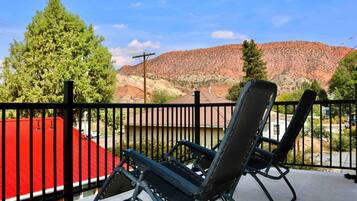 A balcony with two black lounge chairs, a red awning, and a view of a red mountain range.