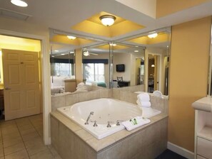 Un bagno spazioso con una vasca da bagno ampia, uno specchio e un ingresso verso un'altra stanza.