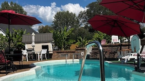 A swimming pool with a metal ladder, surrounded by lounge chairs and red umbrellas. - Experience Charleston charm near Hiwassee River (Charleston)