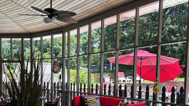 A covered outdoor seating area with a red sofa, black wicker furniture, and a ceiling fan. - Experience Charleston charm near Hiwassee River (Charleston)