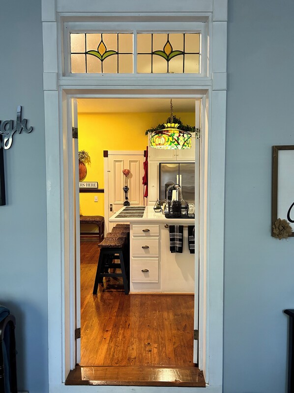 A kitchen with a white countertop, a hanging light fixture, and a wooden stool.