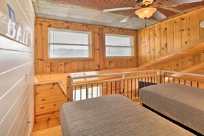 Une cabane avec deux lits, des murs en bois, un escalier et un ventilateur de plafond.