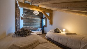 A cozy bedroom with two beds, wooden beams, a rustic ceiling, and a small window.