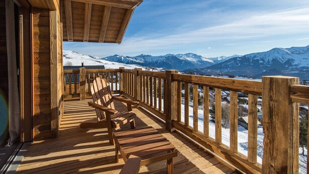A wooden deck with a wooden chair, overlooking a snowy mountain landscape.