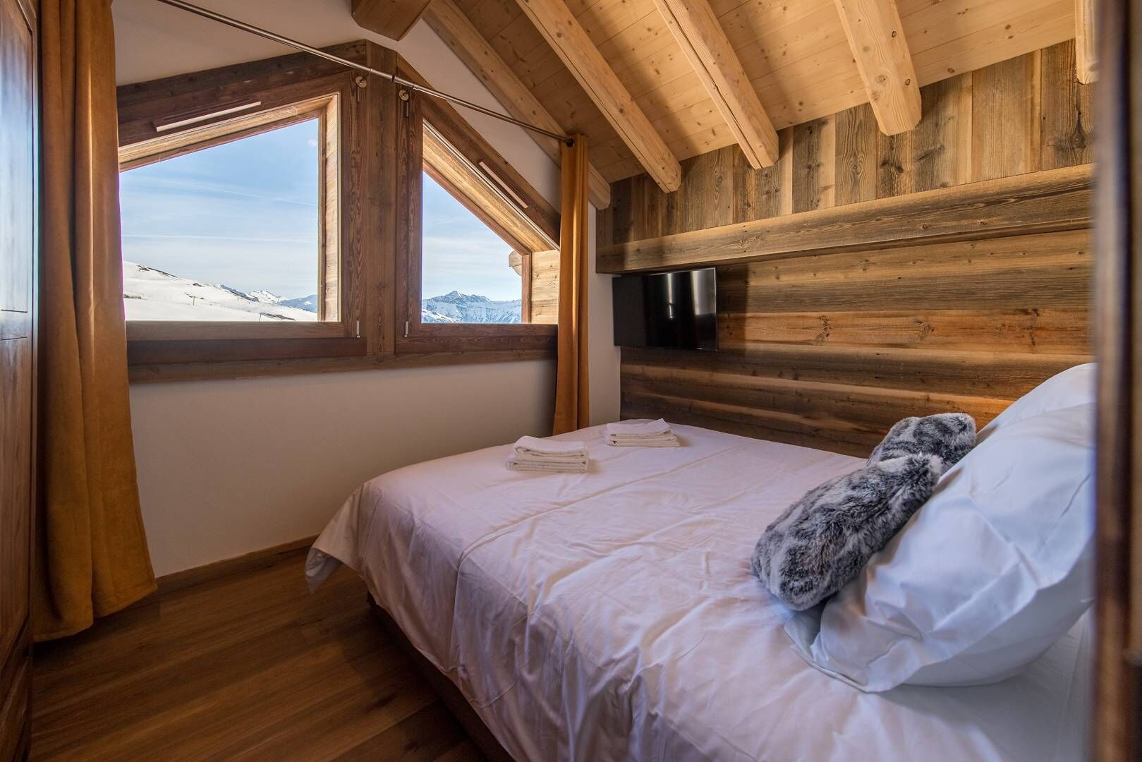 Ein Schlafzimmer mit Bett, einem Fenster mit Bergblick, Holzwänden und einem an der Wand befestigten Flachbildfernseher.